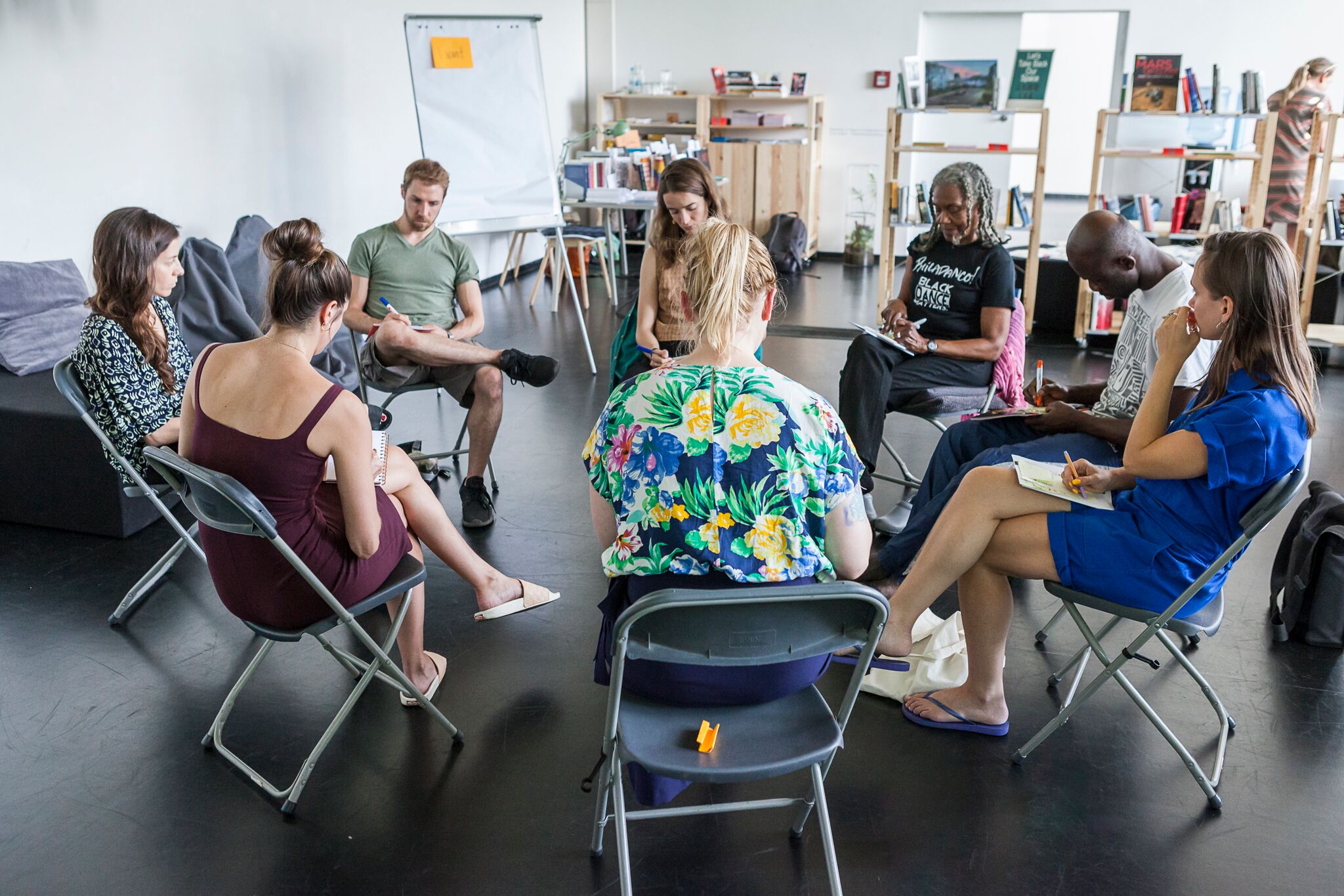 People sit in chairs in a circle inside a dance studio.